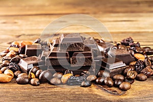 Dark chocolate cubes, coffee beans, peanuts and raisins on wooden table, close-up