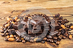 Dark chocolate cubes, coffee beans, peanuts and raisins on wooden table, close-up