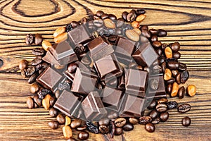 Dark chocolate cubes, coffee beans, peanuts and raisins on wooden table, top view