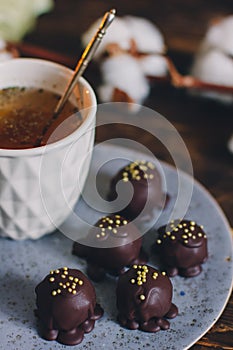 Dark chocolate handmade candy balls on handmade plate on dark wooden background with the cup of tea in a white cup