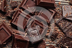Dark chocolate pieces and bar on a brown table. Top view.