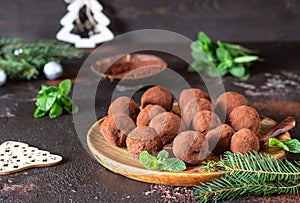 Dark chocolate truffles with raw cocoa powder, mint and fir tree branches, dark brown stone background. Christmas composition