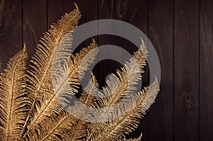 Dark christmas background with golden glittering decorative feathers on glowing garland on brown wooden table as festive border.