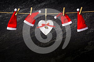 Dark christmas background with santa hats on a rope and wooden heart