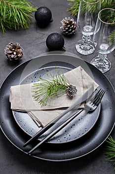 Dark christmas table setting design. Black plates, champagne glasses, fork and knife set with napkin, fir branch