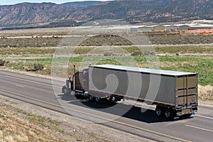 Dark Classic semi truck and trailer on the road with nature view