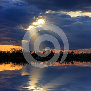 Dark clouds with sun rays over lake