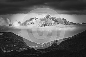 Dark and cloudy sky envelops a majestic mountain range, framed by a lush forest, Tyrol, Austria