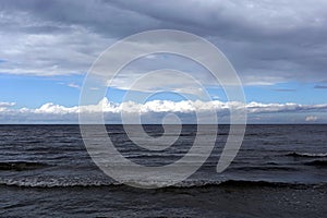 Dark cold waves of the Baltic Sea with layer of white clouds on skyline on a overcast day
