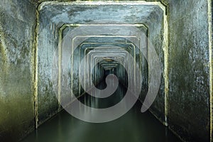 Dark and creepy flooded underground sewer concrete tunnel. Industrial wastewater and urban sewage flowing throw the tunnel