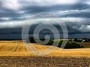 Dark cumulonimbus clouds bringing heavy rain over harvested agrarian fields