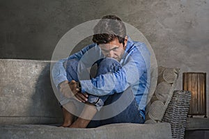 Dark and dramatic lifestyle portrait of attractive depressed and worried man at home couch during covid-19 virus outbreak home