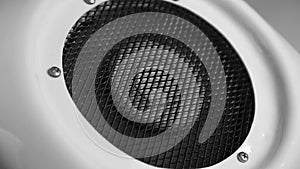 Dark dusty fan blades begin to rotate and gradually increase speed in the white case behind the black grill