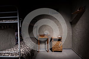 Dark empty jail cell with iron bunk bed and bedside table