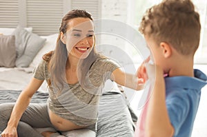 Dark-eyed smiling pregnant woman touching nose of son