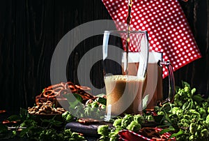 Dark German beer is poured into a glass, fresh green hops and bowls with salty snacks and nuts, autumn beer festival concept, dark