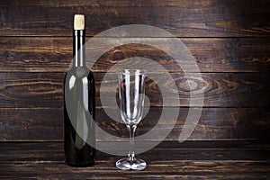 Dark glass wine bottle without label and empty transparent wineglass on brown wooden board background
