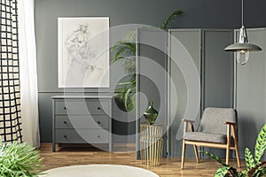 Dark, gray living room interior with a sketch hanging above a wooden chest of drawers next to a screen, golden table and armchair