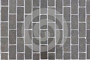 Dark gray paving slabs as background with snow stipes between blocks top view closeup