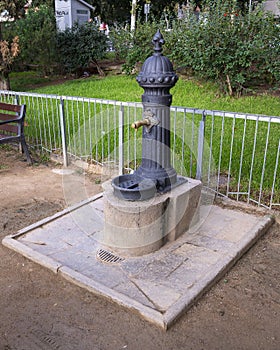 Dark gray water hydrant with push button access and stone pedestal in a park near the Nativity entrance of Sagrada Familia.