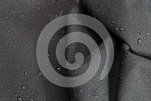 Dark gray waterproof hydrophobic crumpled cloth closeup with rain drops selective focus background