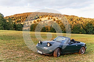 Dark green convertible on a summer meadow with trees photo