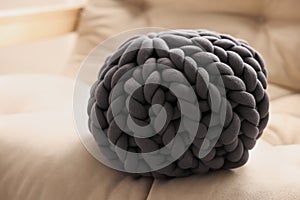 Dark grey chunky knitted pillow on beige sofa, closeup