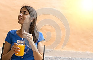 Dark hair Teen thinking and drinking smoothie orange juice with pleasure in a terrace. Happy good looking girl refreshing and