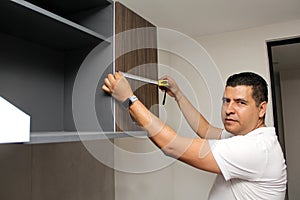 Dark-haired 40-year-old Latino man takes measurements of newly installed kitchen cabinets as a worker