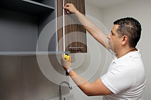 Dark-haired 40-year-old Latino man takes measurements of newly installed kitchen cabinets as a worker