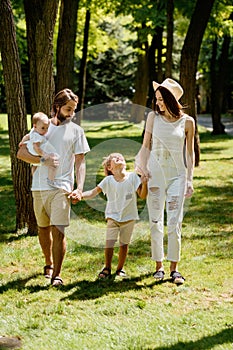 Dark-haired beautiful woman wears the white stylish clothes and hat walks with handsome father and children in the