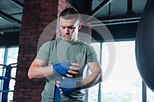 Dark-haired boxer using wrist wraps in gym