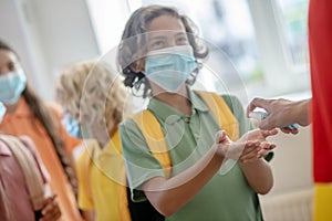 Dark-haired boy in preventive mask getting some sanitizer into his hand