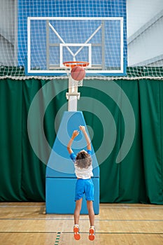 Dark-haired boy in sportswear throwing the ball into the ring