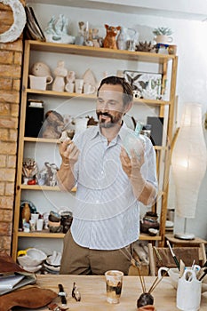 Dark-haired ceramist standing near shelve stand with his handiwork