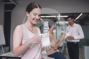 Dark-haired female opening chinese food box, her male colleagues having lunch behind her