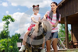 Dark-haired girl enjoying horse riding with her caring mother