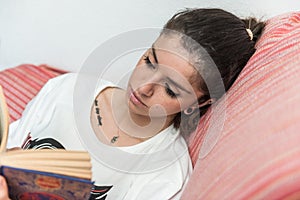 Dark-haired girl quietly reads a book sitting on the couch.