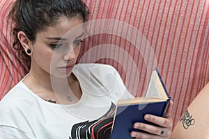 Dark-haired girl quietly reads a book sitting on the couch.