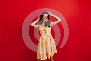 Dark-haired good-humored girl relaxed posing on red background. Woman in bright summer outfit smiling.