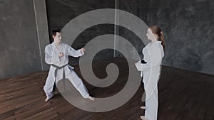 A dark-haired guy and a blonde girl are training martial arts in the gym. Sparring or single duels in taekwondo school