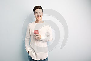 Dark-haired guy dressed in a white long sleeve t-shirt and jeans holds a red plastic cup in his hand on a white