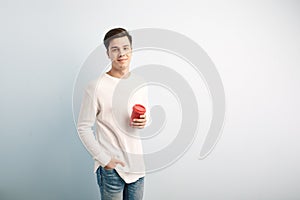 Dark-haired guy dressed in a white long sleeve t-shirt and jeans holds a red plastic cup in his hand on a white