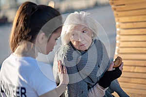 Dark-haired kind volunteer supporting aged homeless woman