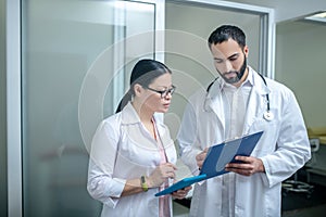 Dark-haired male and female doctors standing in the room together discussing tests results