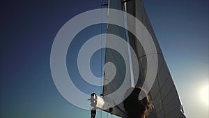 Dark-haired man is correcting huge sails on a sailboat in sunny day.