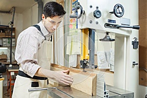 Dark-haired man holding timber on band saw