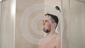 Dark haired man is relaxing in a shower in evening, standing under water flows