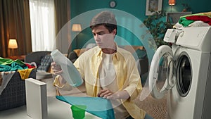 Dark-haired man sitting next to a washing machine, pouring a liquid detergent into a cup, then into the dispencer