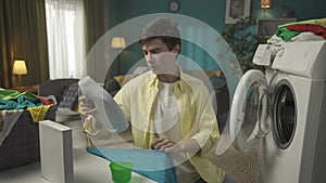 Dark-haired man sitting next to a washing machine, pouring a liquid detergent into a cup, then into the dispenser